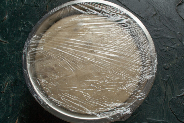 Covering dough with plastic wrap Metal bowl with dough covered tightly with plastic wrap