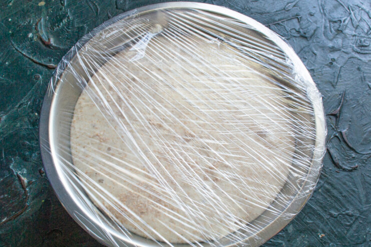 Proofing Dough Under Plastic Wrap Mixing bowl containing dough tightly covered with plastic wrap.