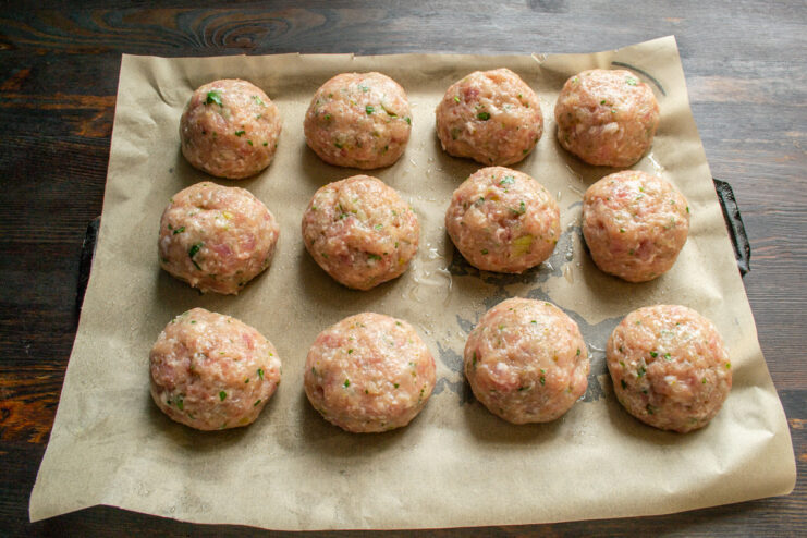 Preparing For Baking Raw meatballs arranged on a parchment-lined baking sheet before going into the oven.