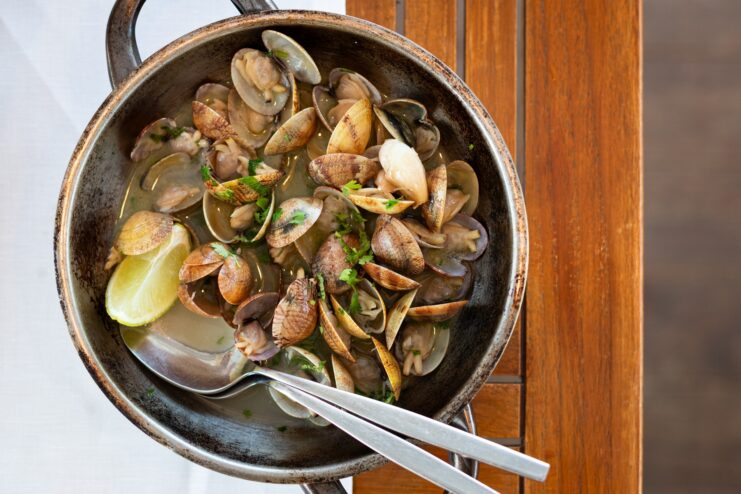 Clams cooking in a pan with white wine, garlic, and fresh cilantro in Bulhão Pato style