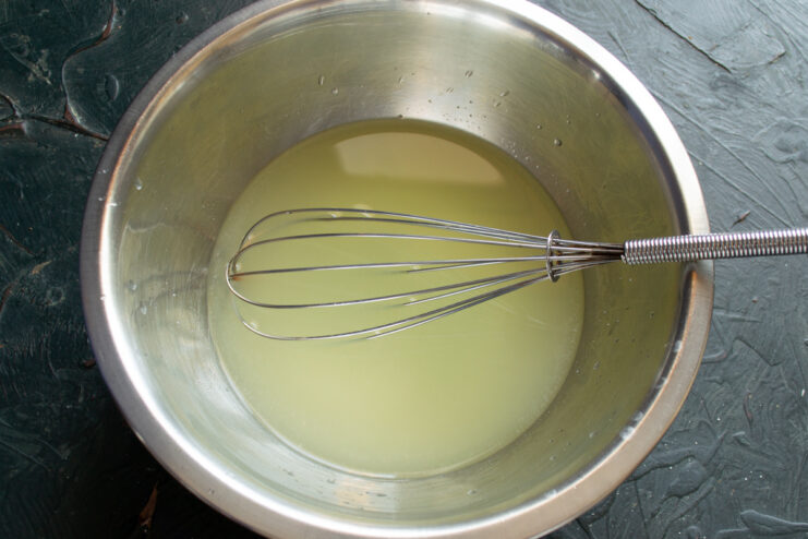 Milk whey in a bowl with a wire whisk