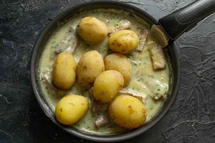 Adding the potatoes Parboiled new potatoes added to a pan with meat and sauce
