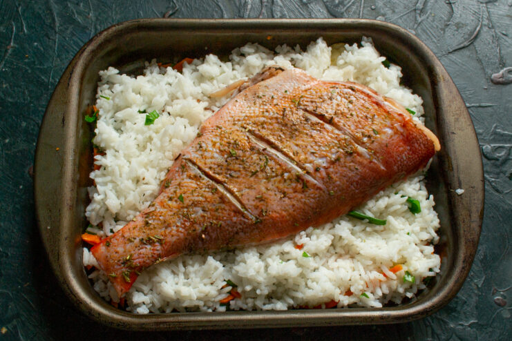 Assembling the Dish Seasoned sea bass placed over a layer of rice in a baking dish