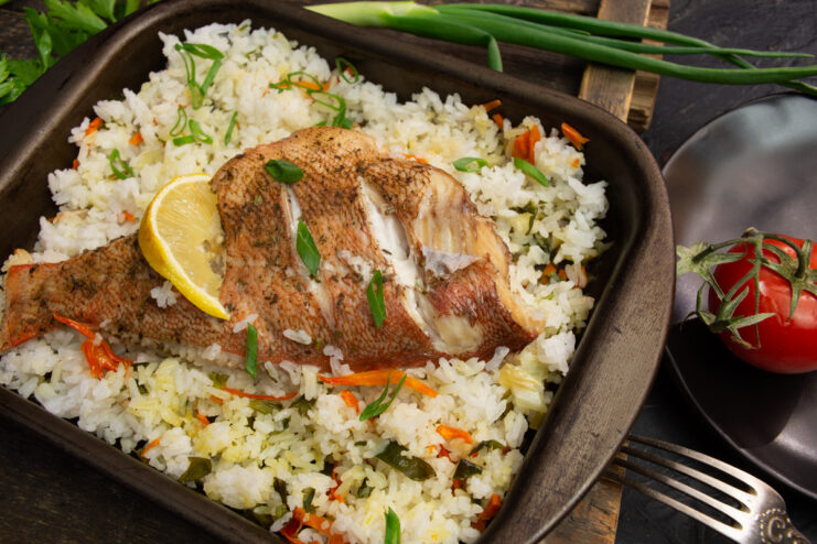 Baked sea bass with rice on a plate garnished with tomato and fresh herbs