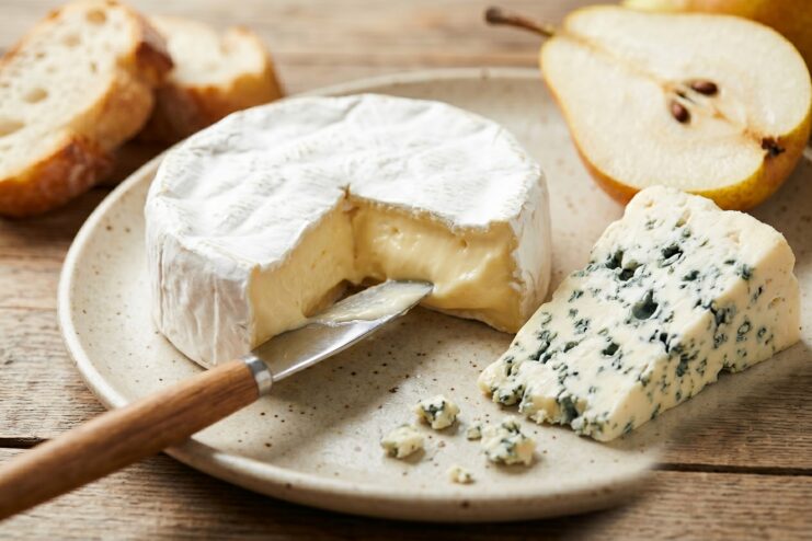 French Camembert And Roquefort Cheeses Soft Camembert with a cheese knife and a wedge of blue Roquefort served on a plate.