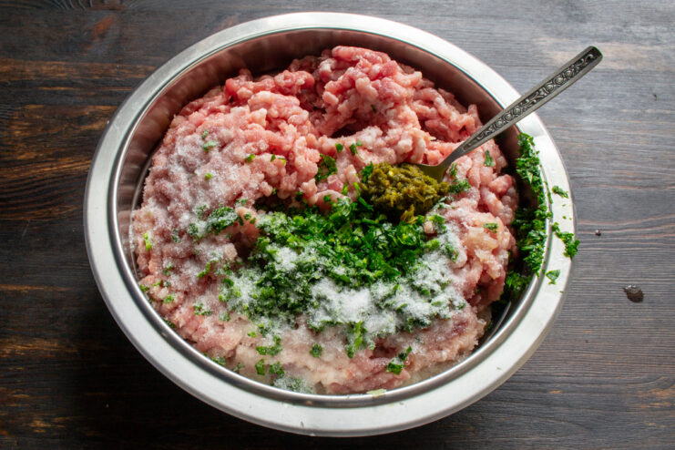Adding Spices And Herbs Ground meat mixture topped with chopped celery, spices, and green adjika paste.
