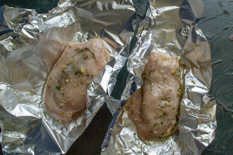 Placing the stuffed chicken on oiled foil Stuffed chicken breast placed on a sheet of oiled aluminum foil.