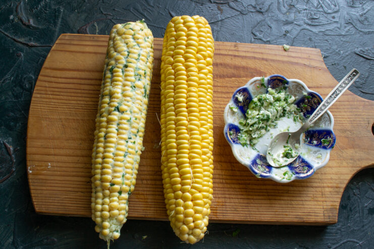 Buttering the corn Spreading thick garlic herb butter over a fresh corn cob