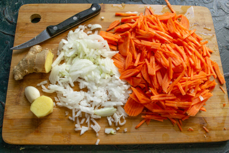Prepping Marinade Veggies Julienned carrots, diced onion, and fresh ginger root on a cutting board.