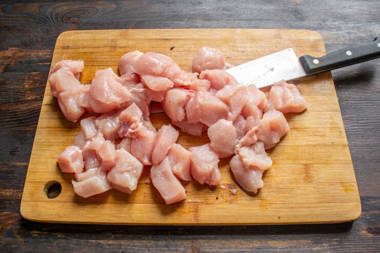 Prepping the chicken Cubed raw chicken breast on a wooden cutting board