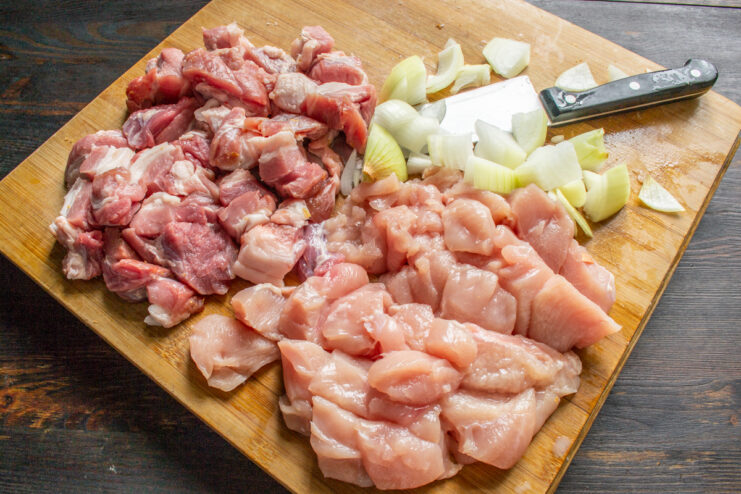 Prepping The Meat Mixture Ingredients Diced raw chicken, pork, and onion resting on a wooden cutting board.