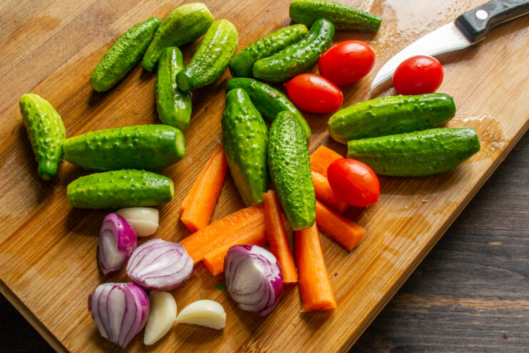 Chopped cucumbers, red onions, garlic, and carrots on a cutting board