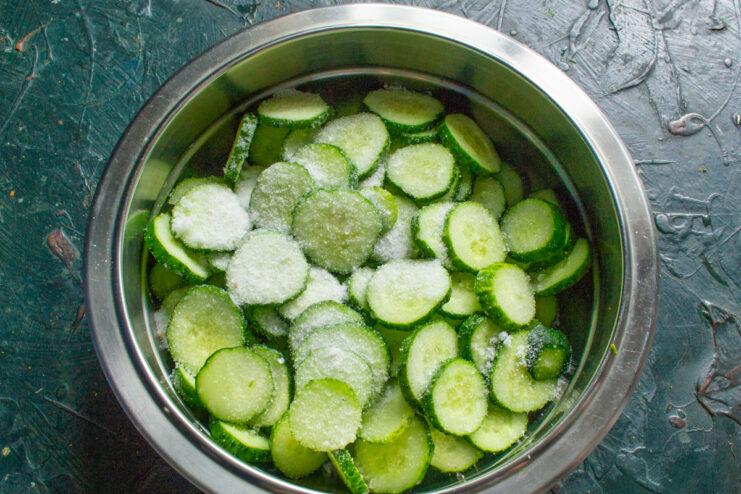 Salting the Cucumbers Sliced cucumbers in a metal bowl sprinkled with salt