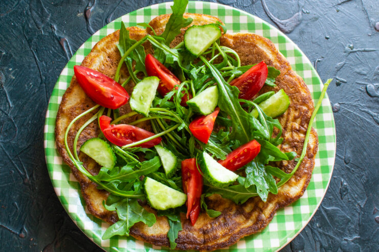 Adding the vegetables Sliced tomatoes and cucumbers arranged on top of arugula on a pancake