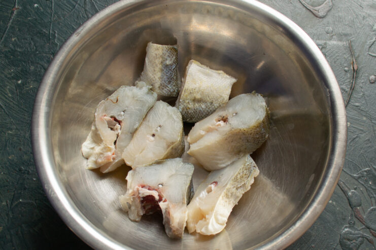 Portioned cuts of fresh white fish meat resting in a metal mixing bowl.