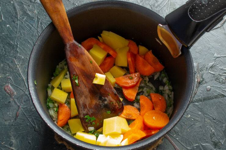 Adding the root vegetables Diced potatoes and sliced carrots mixed with onions in a pot
