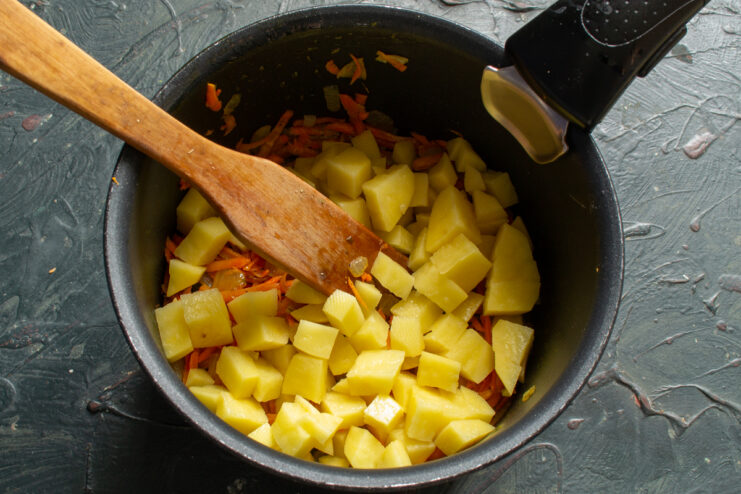 Adding the potatoes Diced potatoes added to the sautéed vegetables in a pot.