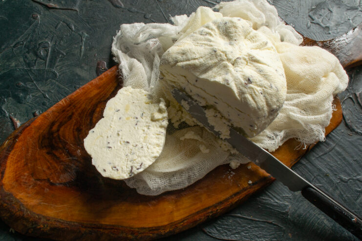 Texture of the finished farmer's cheese Sliced piece of creamy caraway cheese resting on a wooden board
