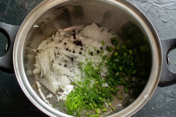 Preparing vegetables for the broth Chopped onions, garlic scapes, and spices inside a soup pot.