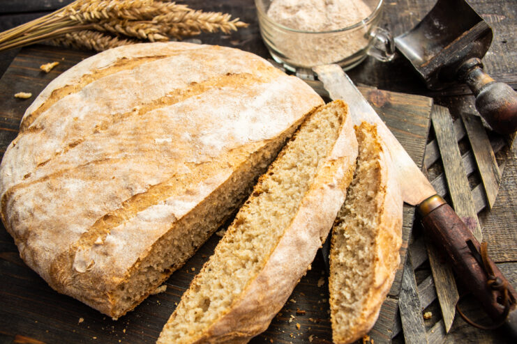 Sliced whole wheat bread resting on a wooden board next to wheat stalks.