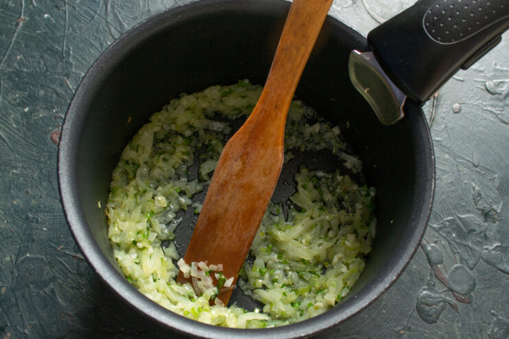 Freshly chopped celery being sauteed alongside onions inside a heavy-bottomed pot.