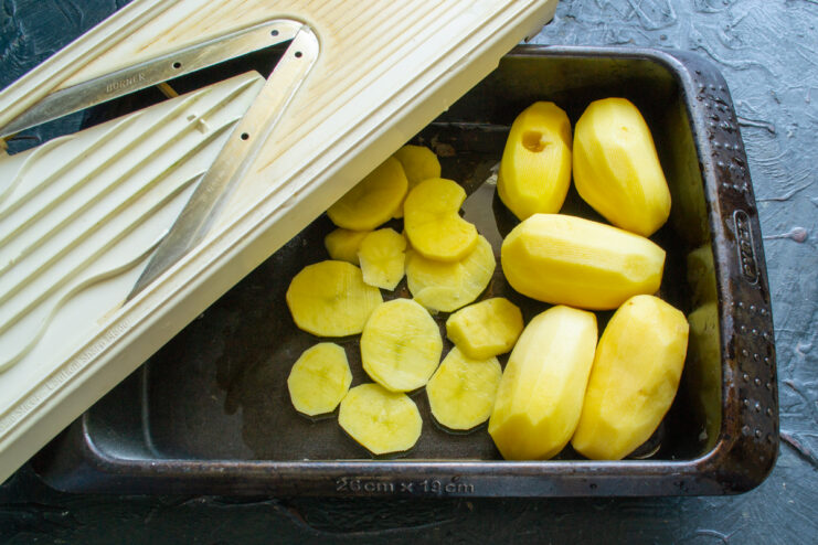 Slicing potatoes into thin identical rounds using a mandoline slicer