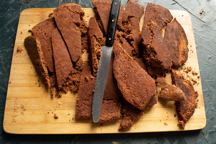 Cutting chocolate sponge cake into pieces on a wooden board.