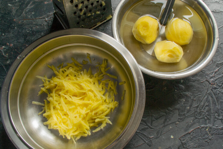 Grating potatoes for the batter Fresh shredded potatoes sitting in a metal mixing bowl