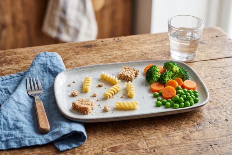 Half-eaten child's lunch with pasta, broccoli, peas, and breadcrumbs on a plate