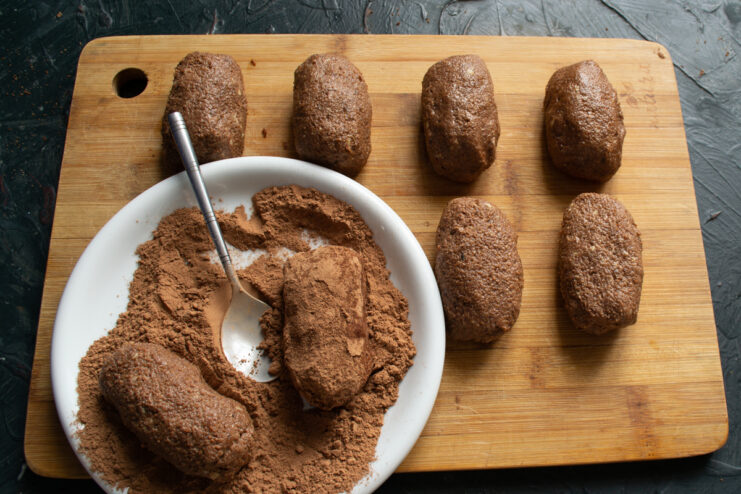 Rolling chocolate pastries in cocoa powder.
