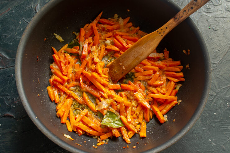 Golden browned carrot batons and onions cooking in a pan