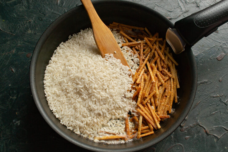 Toasting long-grain white rice and crushed dry noodles in a hot skillet