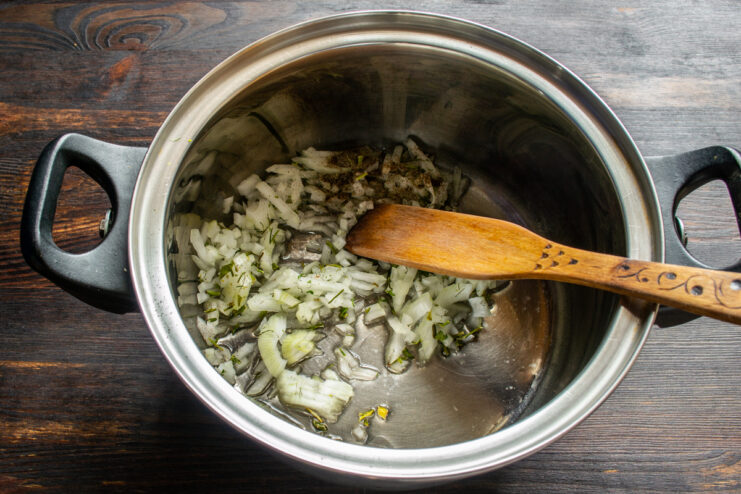 Sautéing chopped onion, garlic, and fresh herbs in a pot with oil