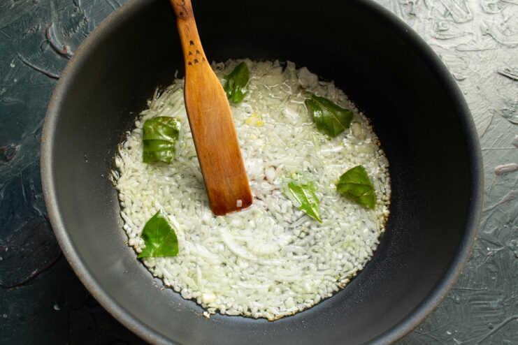 Sautéing chopped onions and bay leaves in a pan with melted ghee