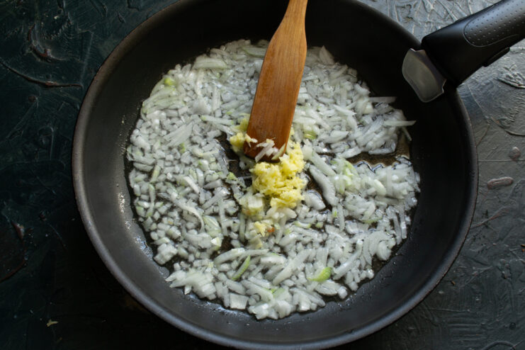 Sautéing Aromatics Sautéing onions and grated ginger in a skillet using a wooden spatula.
