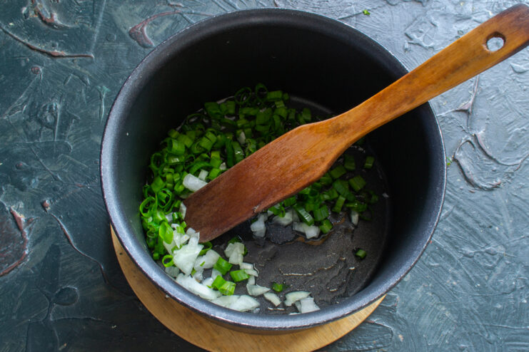 Sautéing freshly chopped green onions in butter inside a heavy-bottomed saucepan