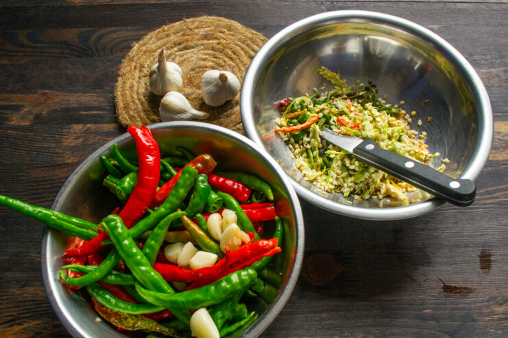 Prepping vegetables for adjika Deseeded peppers and peeled garlic cloves in metal bowls on a wooden table.