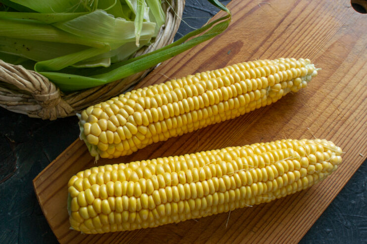 Prepping the corn cobs Cleaned corn on the cob resting on a wooden cutting board