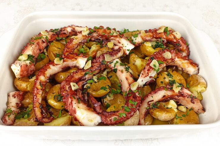 Roasted octopus tentacles and punched potatoes smothered in olive oil in a baking dish