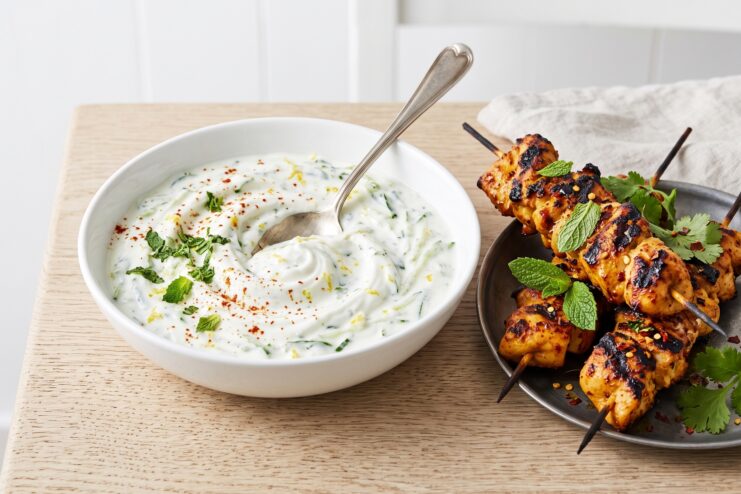 Refreshing yogurt sauce mixed with cucumber and mint in a white bowl paired with chicken skewers.