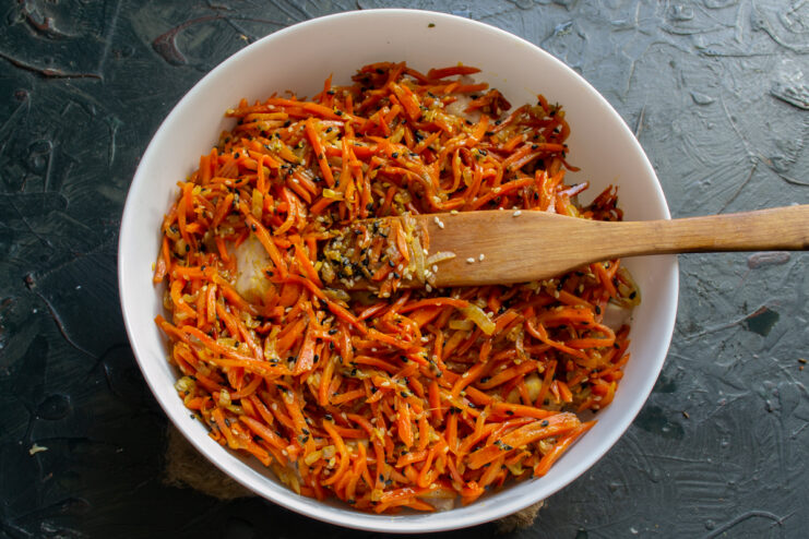Assembling the Dish Spreading vegetable marinade evenly over white fish in a baking dish.