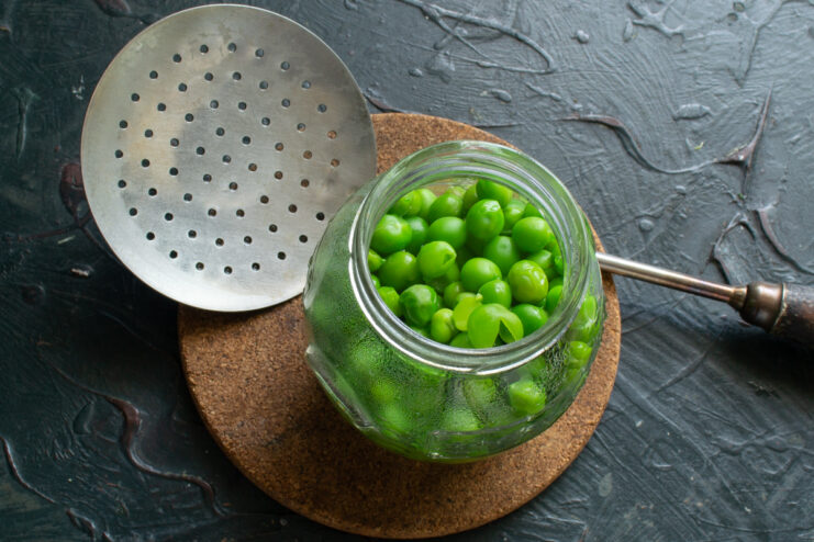 Transferring hot green peas into a sterilized glass jar