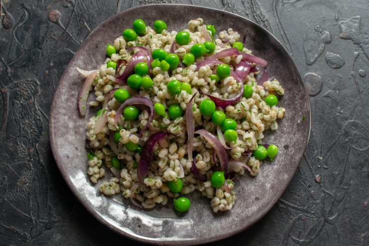 Plating the dish Plated pearl barley with green peas and shallots on a dark dish