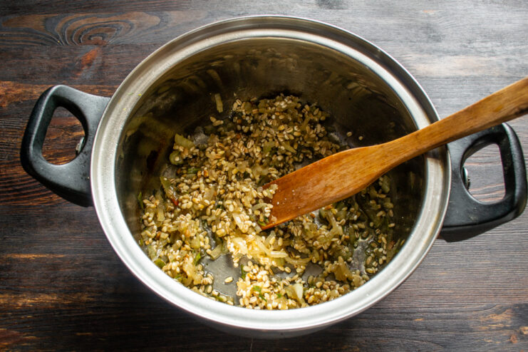 Mixing dry pearl barley into sautéed vegetables in a pot