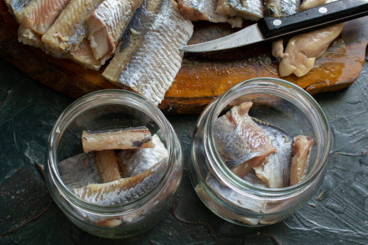 Assembling the appetizer in jars First layer of chopped cured herring fillet placed at the bottom of a glass jar