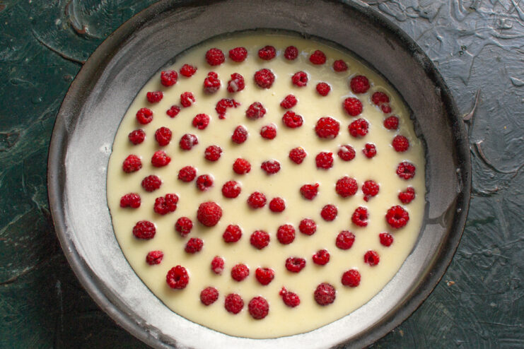 Spreading The First Layer First layer of batter topped with fresh raspberries in a round baking pan