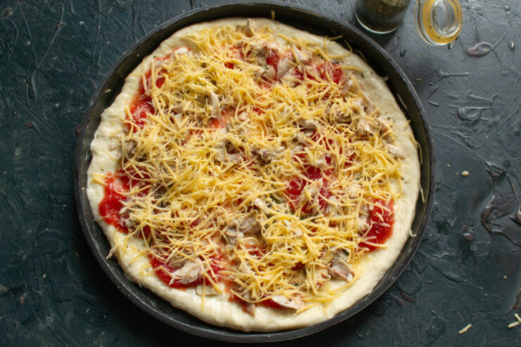 Adding the toppings Pizza crust topped with cooked chicken and grated cheese before baking