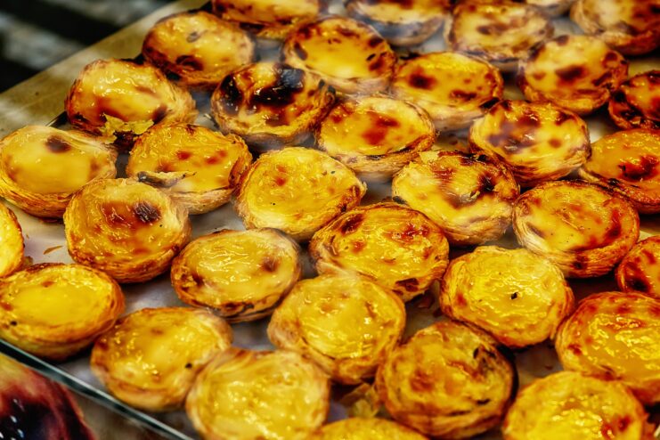 Freshly baked pastel de nata custard tarts with scorched tops sitting on a baking sheet
