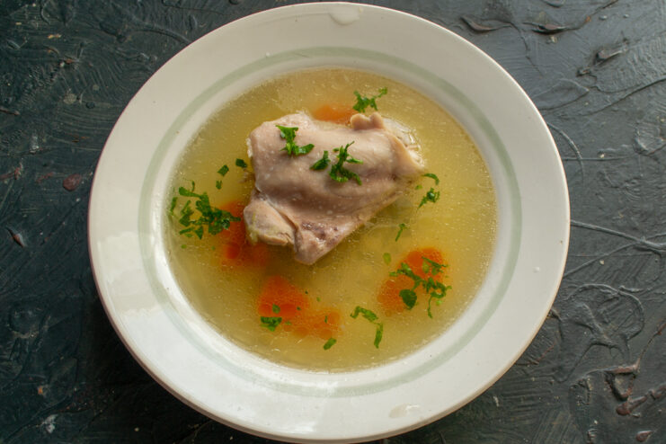 Serving the finished dish Plated chicken broth with meat and fresh herbs in a white bowl