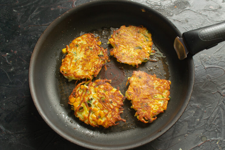 Browning the fritters to a golden crust Golden brown potato fritters sizzling in a frying pan